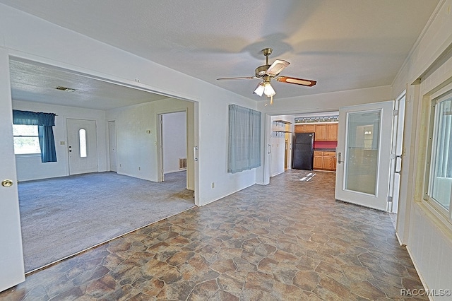 unfurnished living room featuring ceiling fan, dark carpet, and a textured ceiling