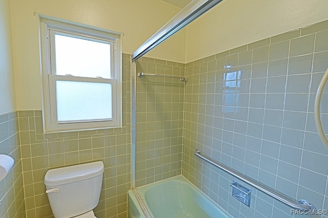 bathroom featuring tiled shower / bath combo, toilet, and tile walls