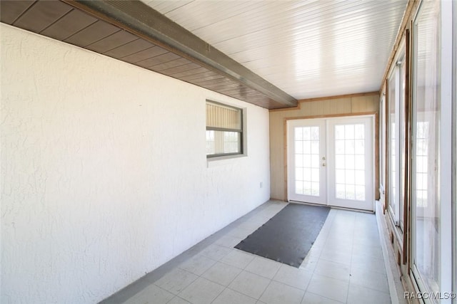 unfurnished sunroom featuring a healthy amount of sunlight, beamed ceiling, and french doors