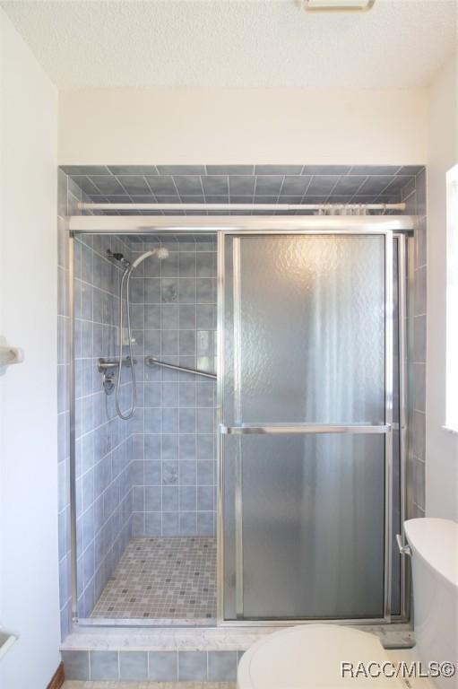 bathroom with a textured ceiling, a stall shower, and toilet