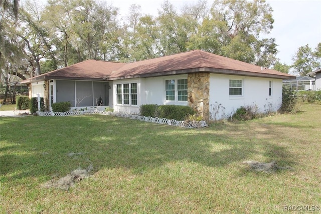 exterior space featuring an attached garage, a sunroom, a yard, stone siding, and stucco siding