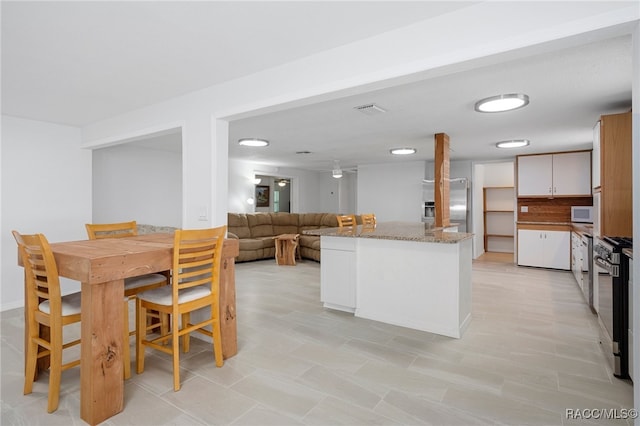 kitchen with white cabinets, backsplash, light stone counters, and stainless steel range oven