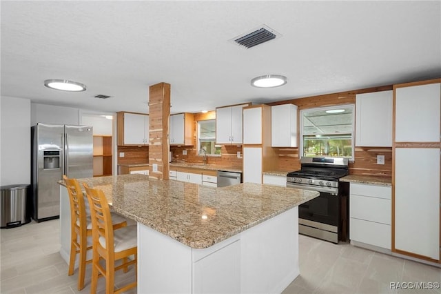 kitchen featuring decorative backsplash, appliances with stainless steel finishes, a center island, and white cabinetry