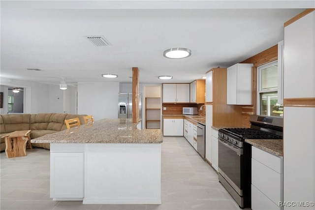 kitchen with white cabinetry, ceiling fan, stainless steel appliances, light stone counters, and a kitchen island