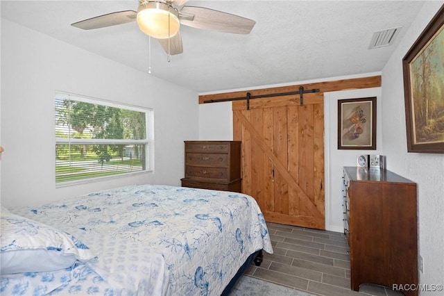 bedroom featuring a barn door, ceiling fan, and dark hardwood / wood-style flooring