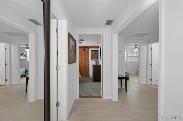 hallway featuring a barn door, a healthy amount of sunlight, and light tile patterned flooring