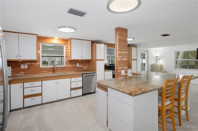 kitchen featuring decorative backsplash, white cabinetry, stainless steel dishwasher, and sink