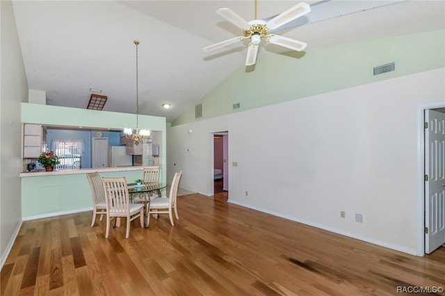 dining area with wood-type flooring, ceiling fan with notable chandelier, and high vaulted ceiling