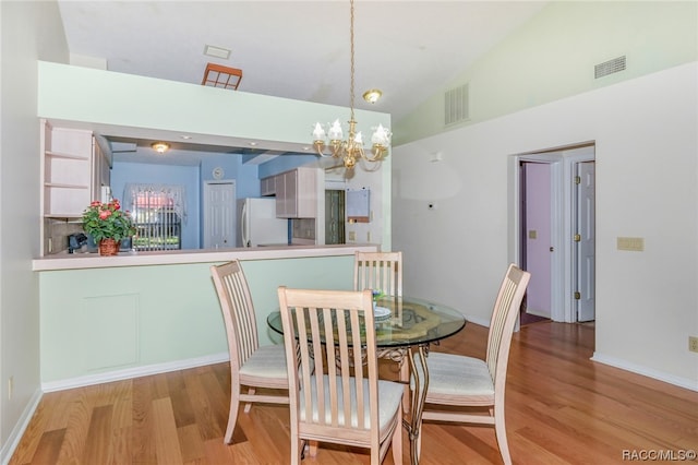 dining area with a notable chandelier, light hardwood / wood-style floors, and high vaulted ceiling