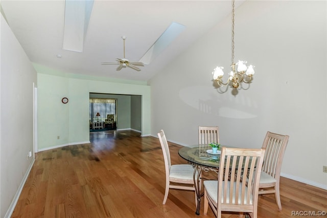 dining area featuring wood-type flooring, ceiling fan with notable chandelier, a skylight, and high vaulted ceiling