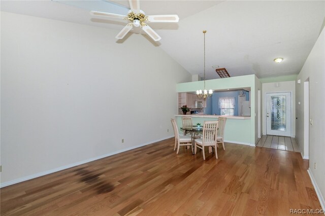 unfurnished dining area featuring ceiling fan with notable chandelier, wood-type flooring, and high vaulted ceiling