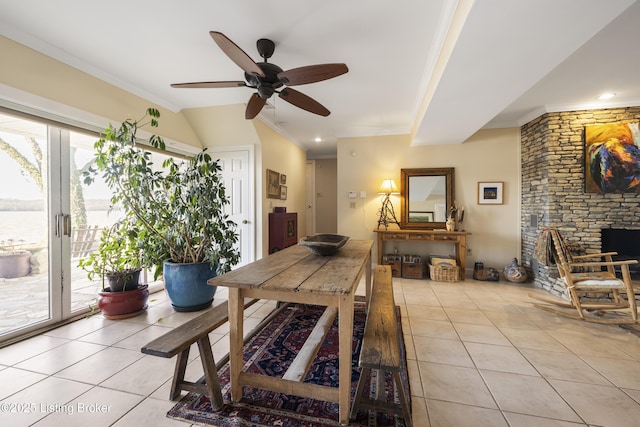 tiled dining area featuring vaulted ceiling, a fireplace, ceiling fan, crown molding, and a water view