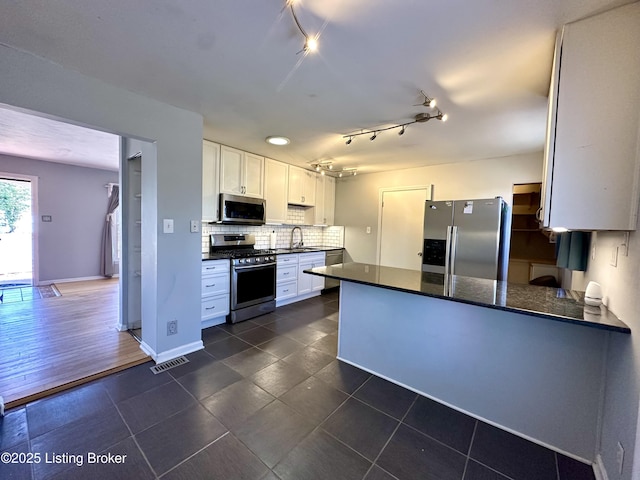 kitchen with appliances with stainless steel finishes, sink, white cabinets, decorative backsplash, and kitchen peninsula