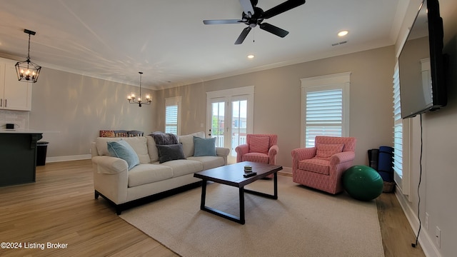 living room with ceiling fan with notable chandelier, ornamental molding, and light hardwood / wood-style flooring