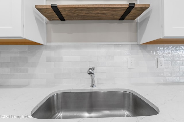 details with tasteful backsplash, white cabinetry, sink, and light stone counters