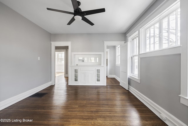 unfurnished living room with dark wood-style floors, ceiling fan, and baseboards