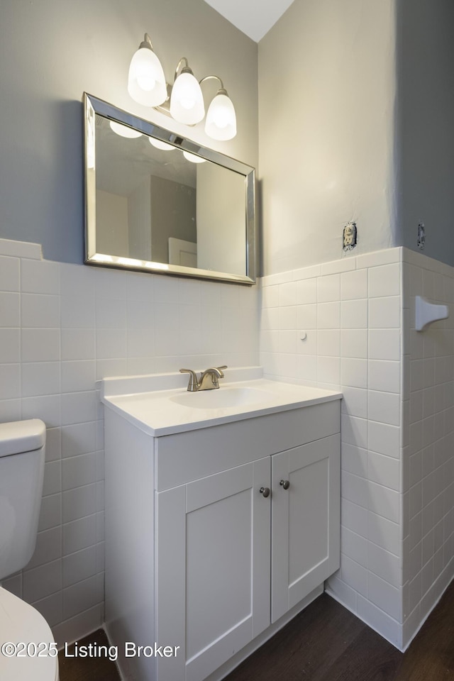 bathroom featuring toilet, wainscoting, tile walls, and vanity