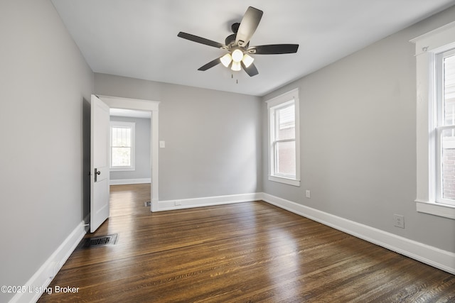 empty room featuring dark wood-style flooring, visible vents, and baseboards