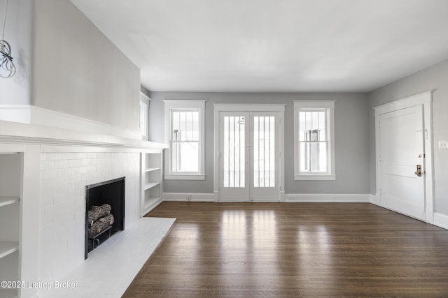 unfurnished living room featuring dark wood-style floors, a brick fireplace, and baseboards