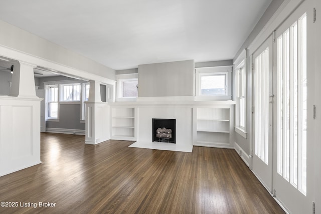 unfurnished living room with plenty of natural light, a fireplace with flush hearth, decorative columns, and dark wood-style flooring