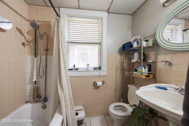 bathroom featuring shower / bathtub combination with curtain, a sink, toilet, and tile walls