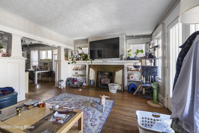 living room featuring a fireplace, a textured ceiling, ornate columns, and wood finished floors