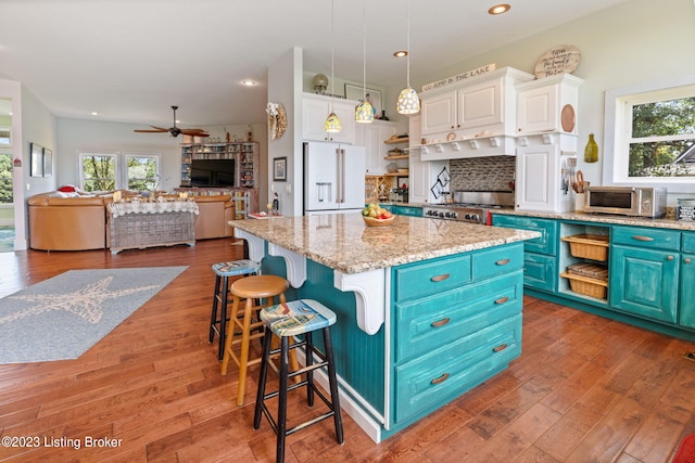 kitchen with ceiling fan, a kitchen island, hanging light fixtures, white cabinets, and high end white fridge