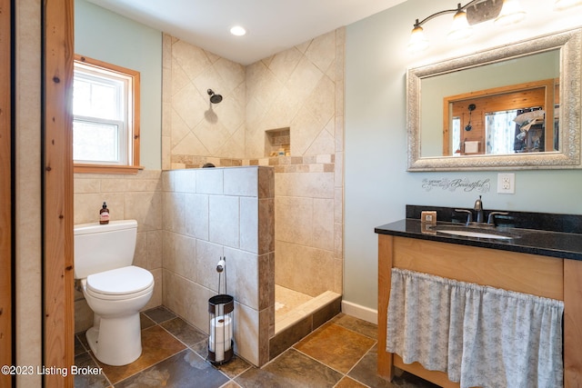 bathroom featuring vanity, tile walls, a tile shower, tile flooring, and toilet