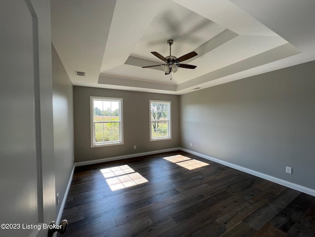 empty room with ceiling fan, dark hardwood / wood-style floors, and a tray ceiling