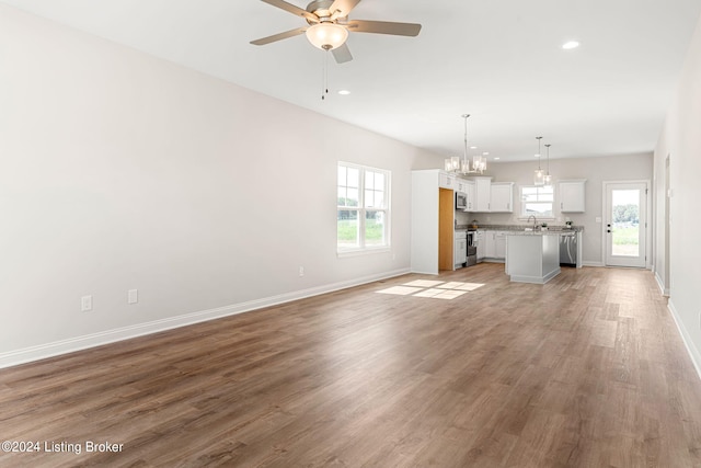 unfurnished living room with light wood finished floors, recessed lighting, baseboards, and ceiling fan with notable chandelier