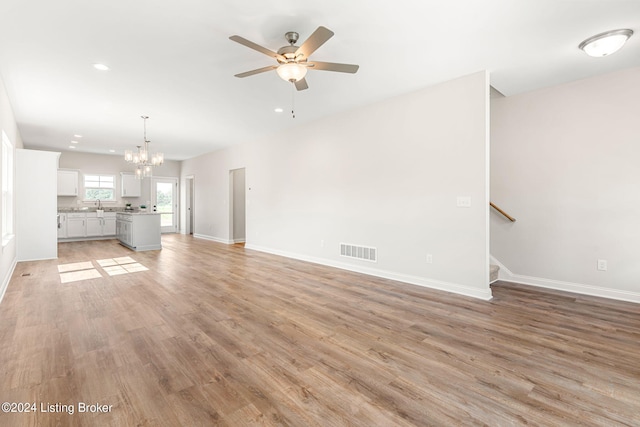 unfurnished living room with stairs, visible vents, light wood-type flooring, baseboards, and ceiling fan with notable chandelier