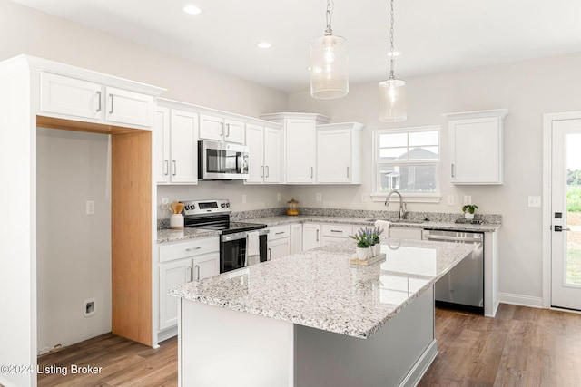 kitchen featuring white cabinets, a kitchen island, wood finished floors, stainless steel appliances, and a sink