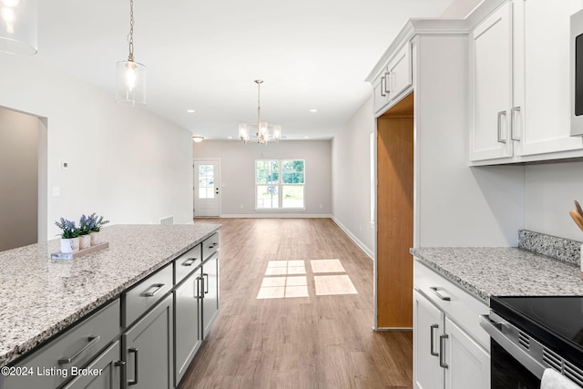 kitchen featuring light stone counters, white cabinetry, hanging light fixtures, and wood finished floors