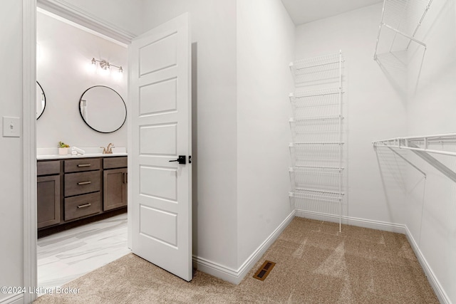 walk in closet with visible vents, a sink, and light colored carpet