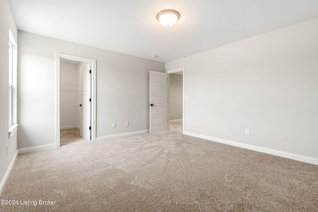 unfurnished bedroom with a closet, light colored carpet, a spacious closet, and baseboards