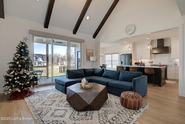 living room with beamed ceiling, light wood-type flooring, sink, and high vaulted ceiling