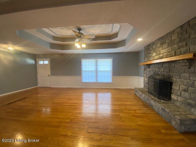 unfurnished living room with a raised ceiling, ceiling fan, a brick fireplace, and wood-type flooring