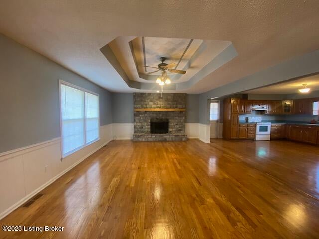 unfurnished living room with ceiling fan, hardwood / wood-style flooring, a raised ceiling, and a brick fireplace