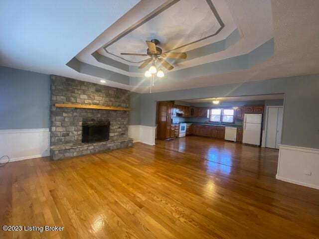 unfurnished living room featuring a raised ceiling, a brick fireplace, hardwood / wood-style floors, and ceiling fan