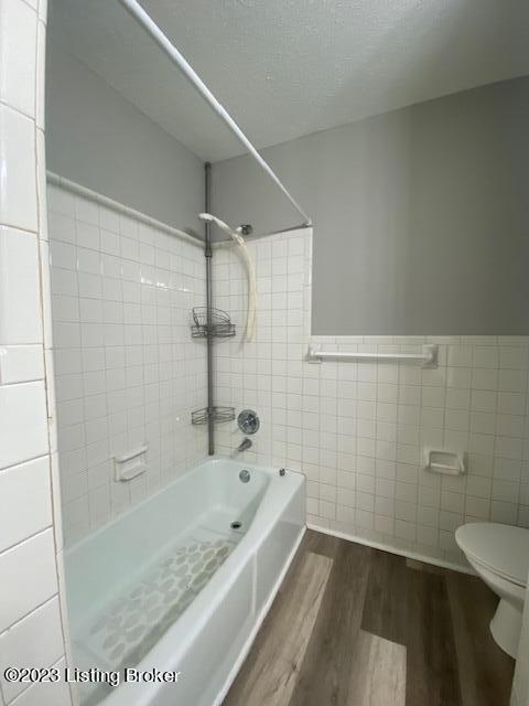 bathroom featuring a textured ceiling, tile walls, toilet,  shower combination, and hardwood / wood-style flooring