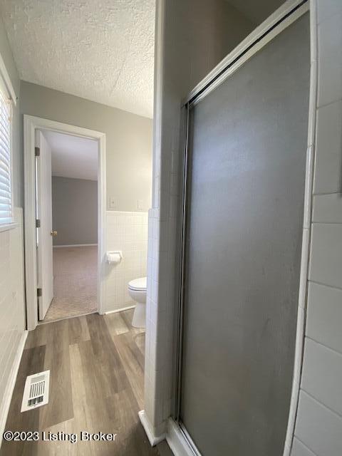 bathroom featuring toilet, an enclosed shower, a textured ceiling, wood-type flooring, and tile walls