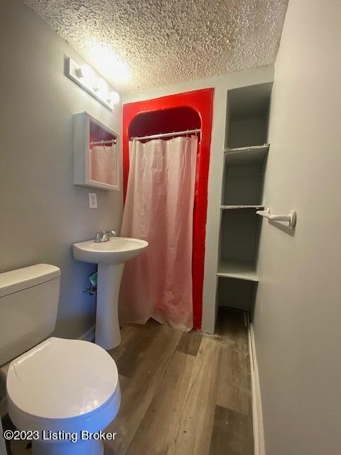 bathroom featuring a shower with curtain, toilet, hardwood / wood-style flooring, and a textured ceiling