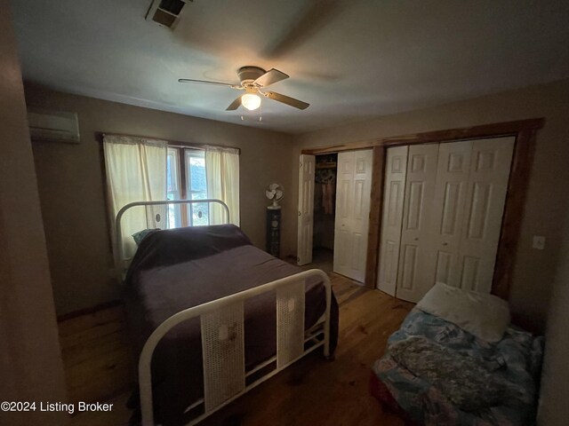 bedroom featuring ceiling fan, an AC wall unit, multiple closets, and hardwood / wood-style flooring