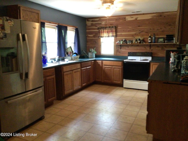 kitchen featuring stainless steel fridge, wooden walls, electric stove, and plenty of natural light