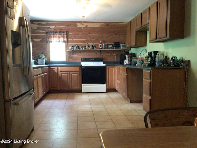 kitchen with stainless steel fridge, electric stove, light tile patterned floors, and wood walls