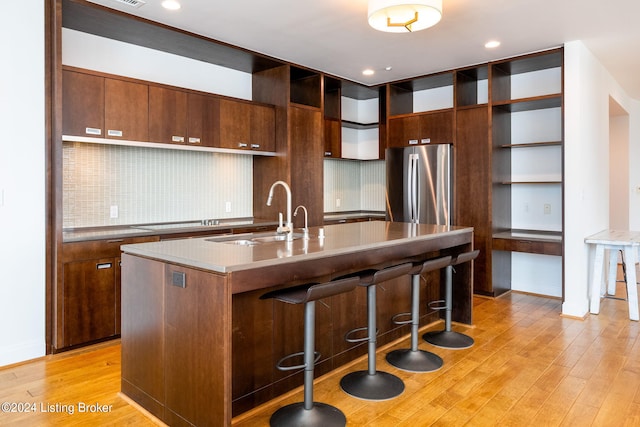 kitchen featuring tasteful backsplash, a center island with sink, a breakfast bar area, stainless steel fridge, and light wood-type flooring