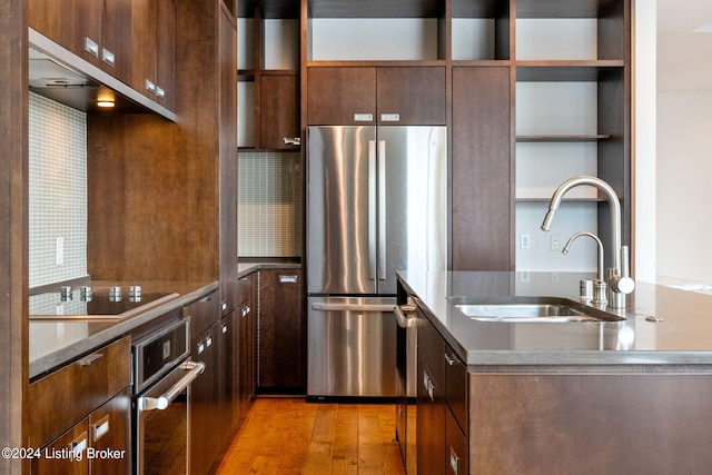 kitchen with backsplash, sink, appliances with stainless steel finishes, and light hardwood / wood-style flooring