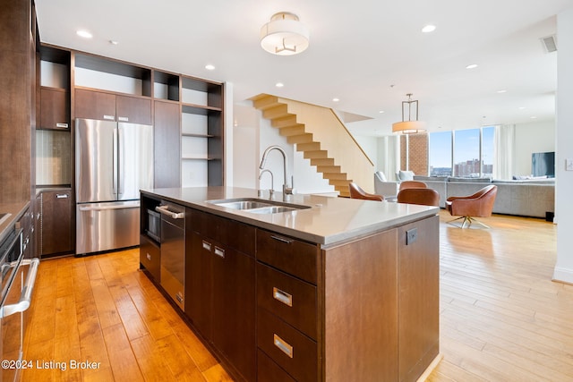 kitchen featuring backsplash, appliances with stainless steel finishes, sink, light wood-type flooring, and a center island with sink