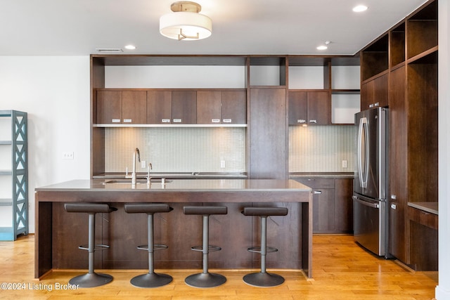 kitchen with a breakfast bar area, stainless steel refrigerator, tasteful backsplash, and light hardwood / wood-style floors