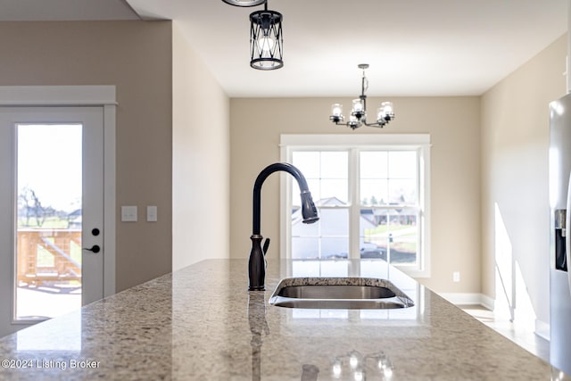 kitchen featuring decorative light fixtures, light stone counters, a healthy amount of sunlight, and a notable chandelier